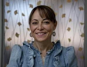 Woman smiling in denim shirt with floral background.